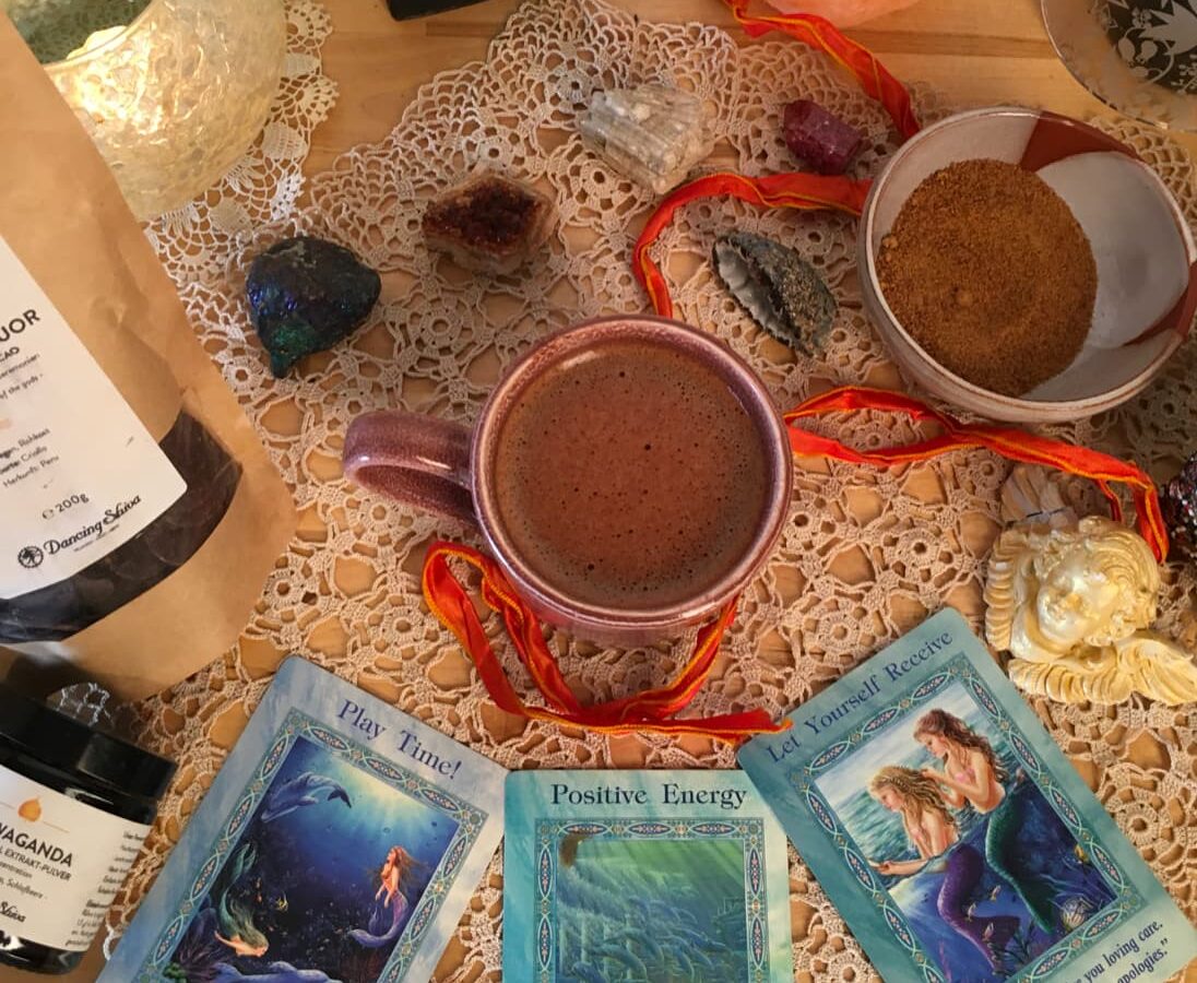 Kakaozeremonie zuhause – Tasse mit zeremoniellem Kakao umgeben von Kristallen, Oracle Cards und Dancing Shiva Produkten