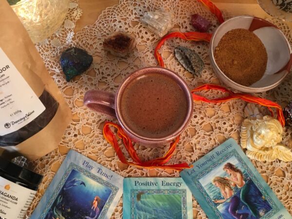 Kakaozeremonie zuhause – Tasse mit zeremoniellem Kakao umgeben von Kristallen, Oracle Cards und Dancing Shiva Produkten