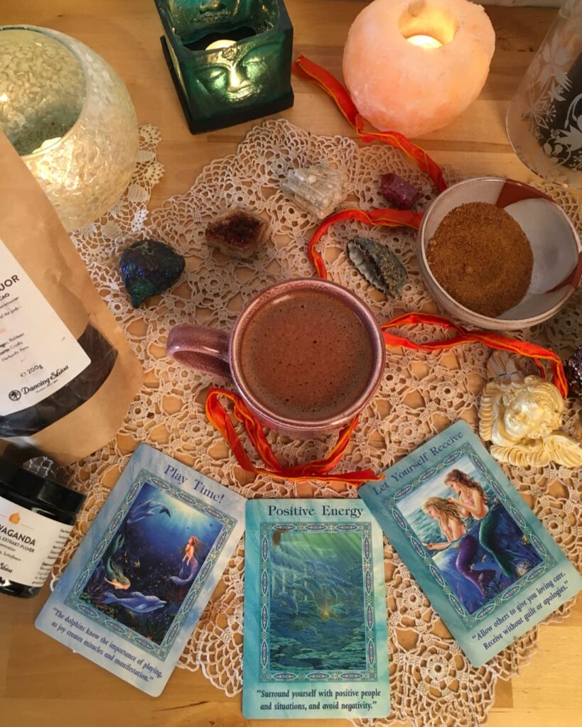 Kakaozeremonie zuhause – Tasse mit zeremoniellem Kakao umgeben von Kristallen, Oracle Cards und Dancing Shiva Produkten